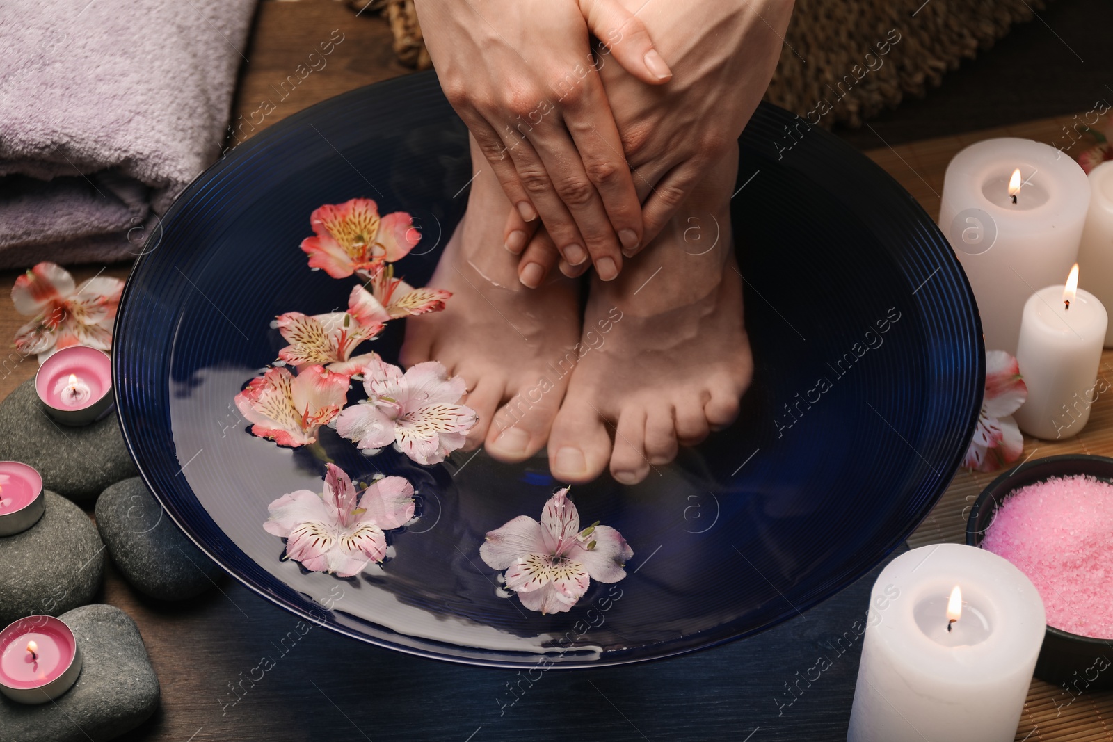 Photo of Woman soaking her feet in bowl with water and flowers on floor, closeup. Spa treatment