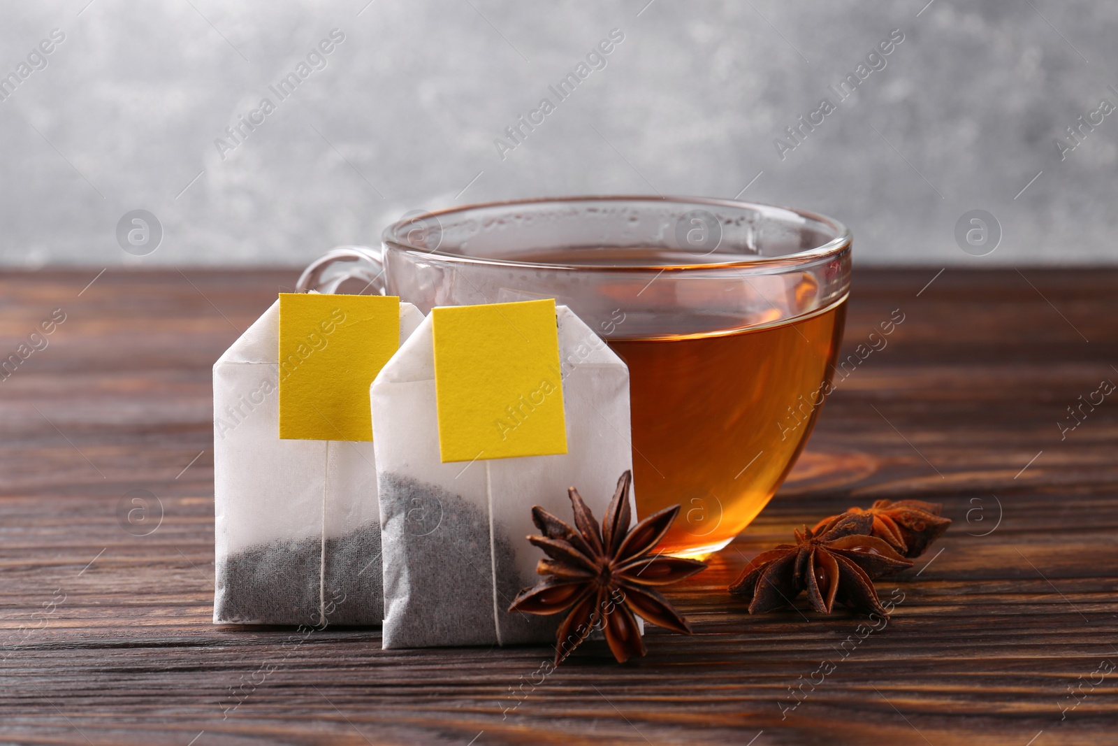 Photo of Tea bags, cup of hot drink and anise stars on wooden table, closeup