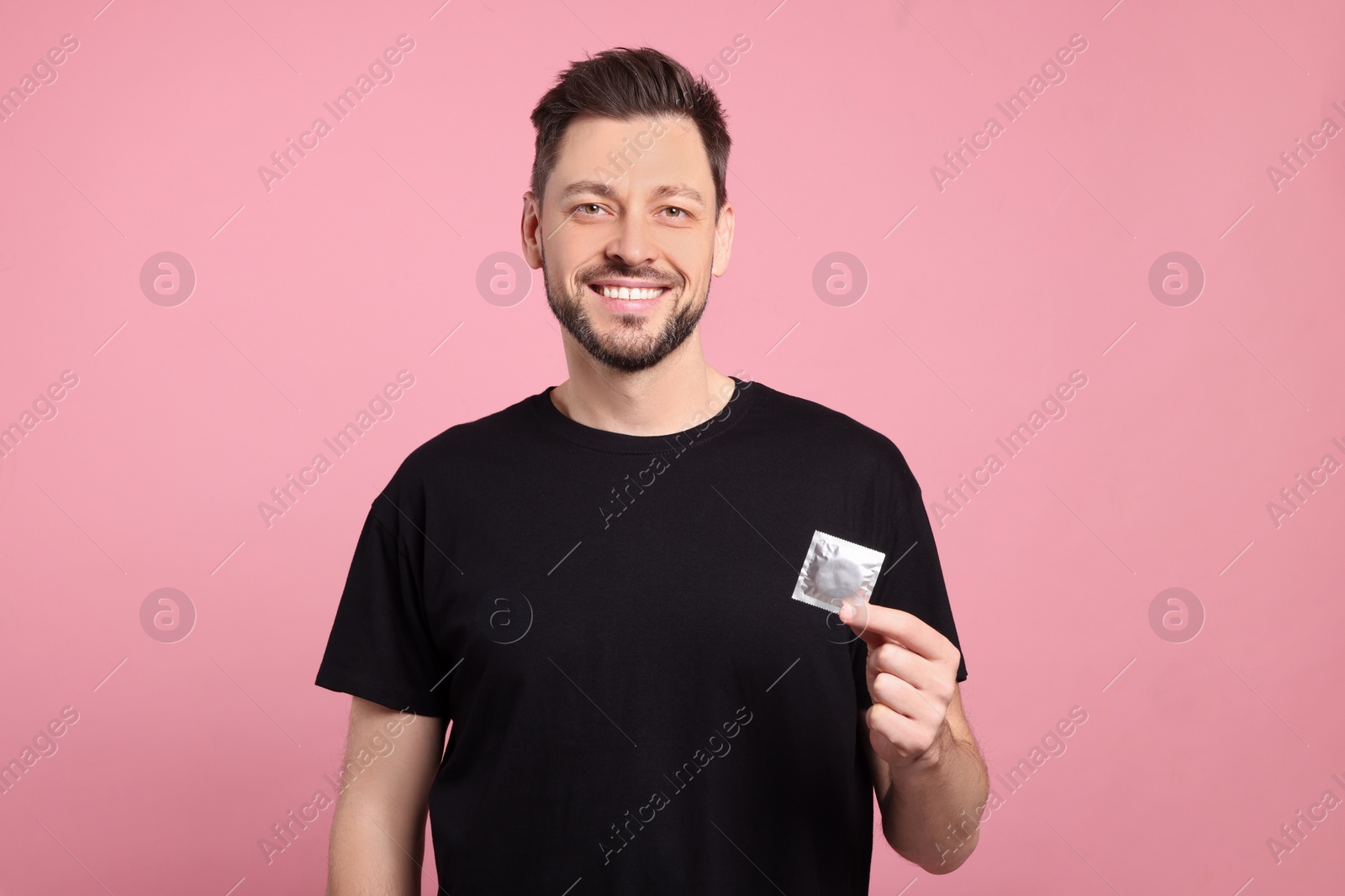 Photo of Happy man holding condom on pink background