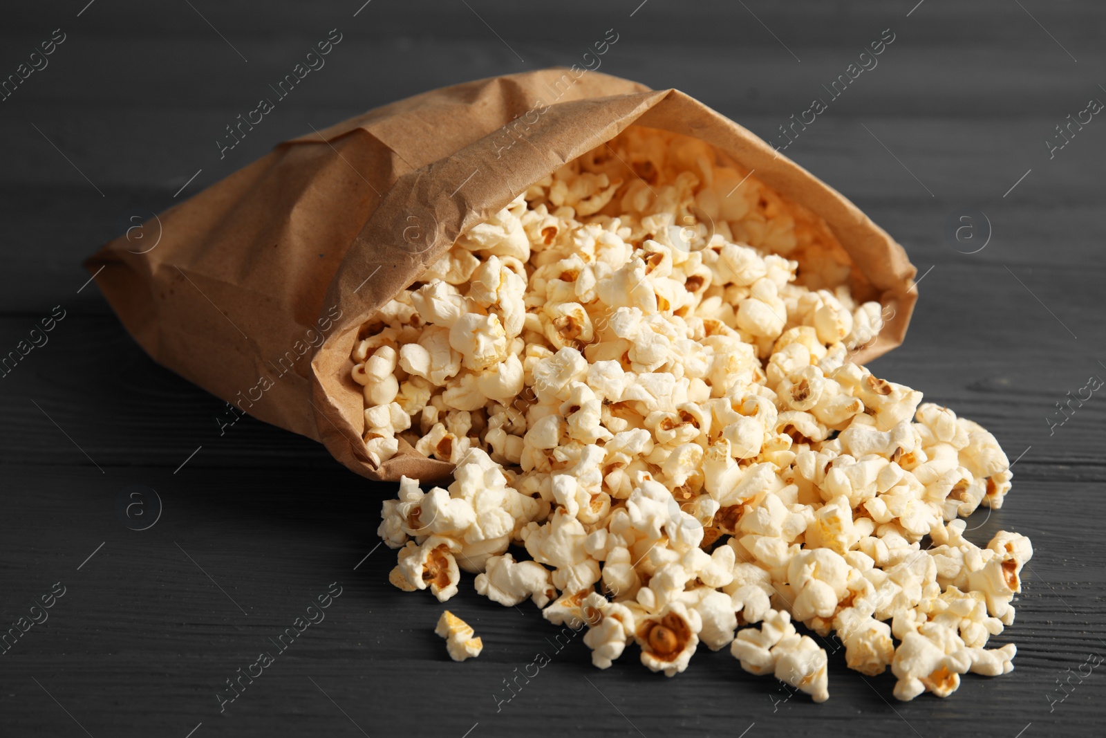 Photo of Paper bag with tasty popcorn on wooden background