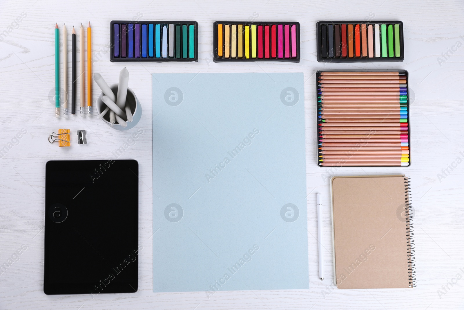 Photo of Layout with blank paper, soft pastels and other drawing supplies on white wooden table at artist's workplace, top view. Space for design