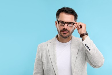 Portrait of man in stylish glasses on light blue background, space for text
