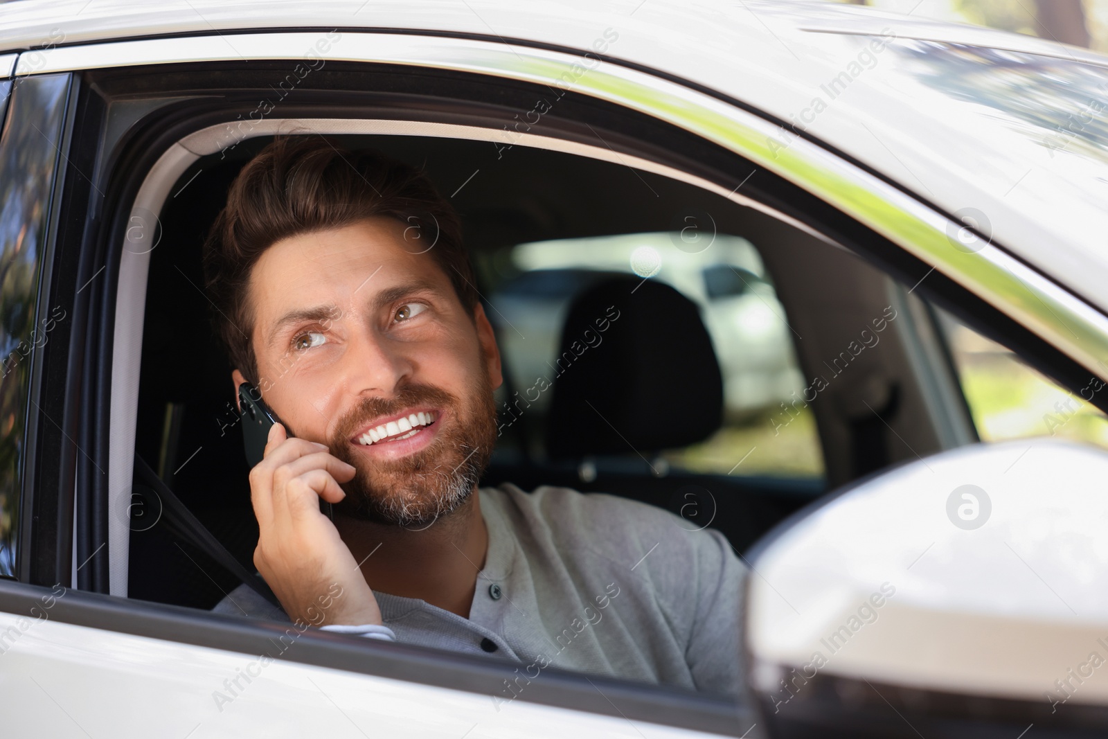 Photo of Happy bearded man talking on smartphone in car, view from outside