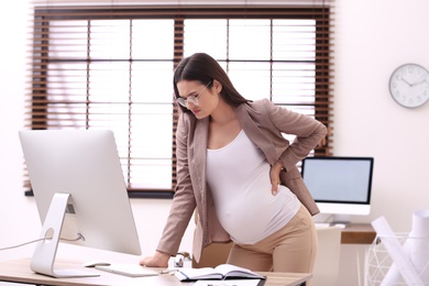 Photo of Young pregnant woman suffering from pain while working in office