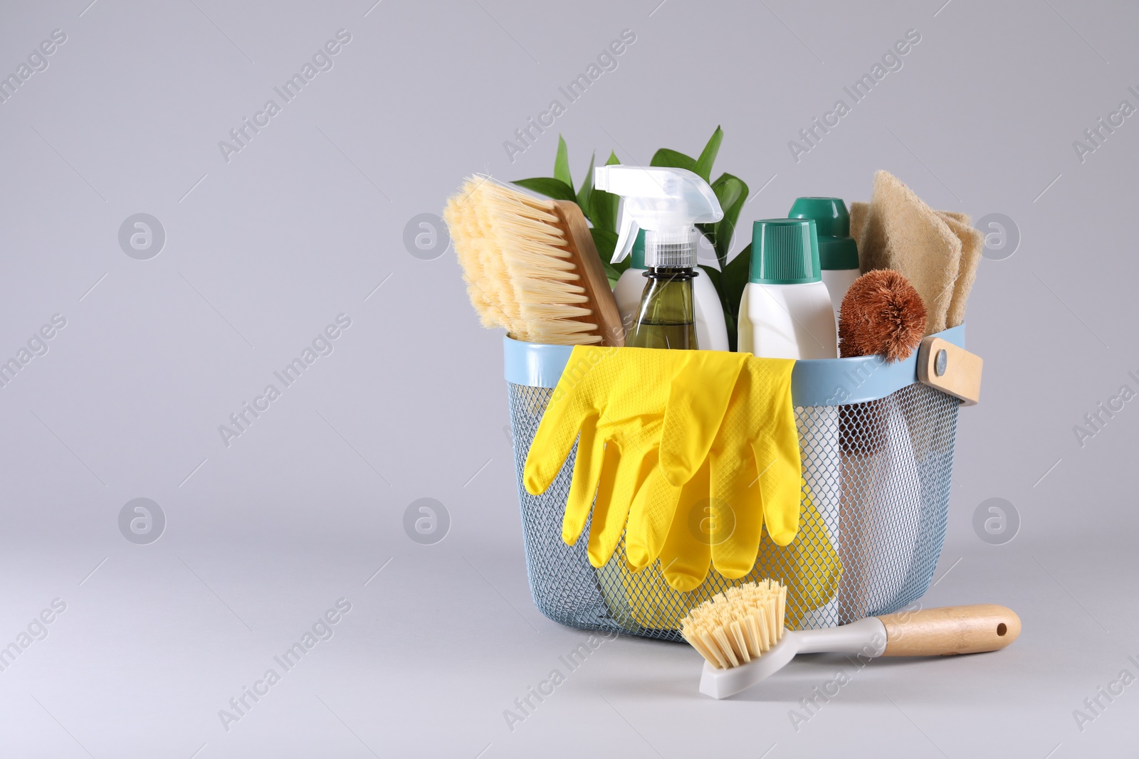 Photo of Set of different cleaning supplies in basket on light grey background. Space for text