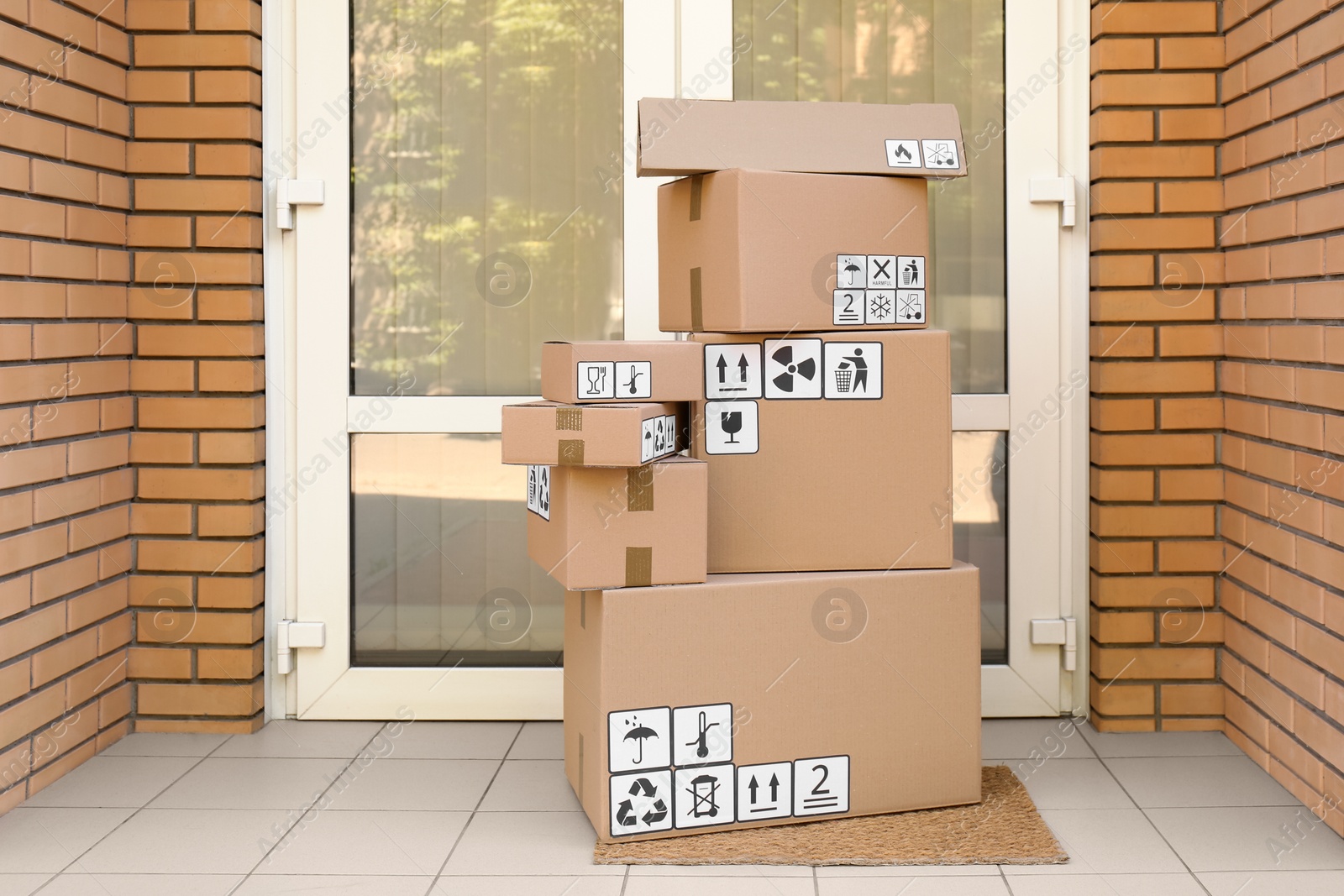 Photo of Cardboard boxes with different packaging symbols on door mat near entrance. Parcel delivery