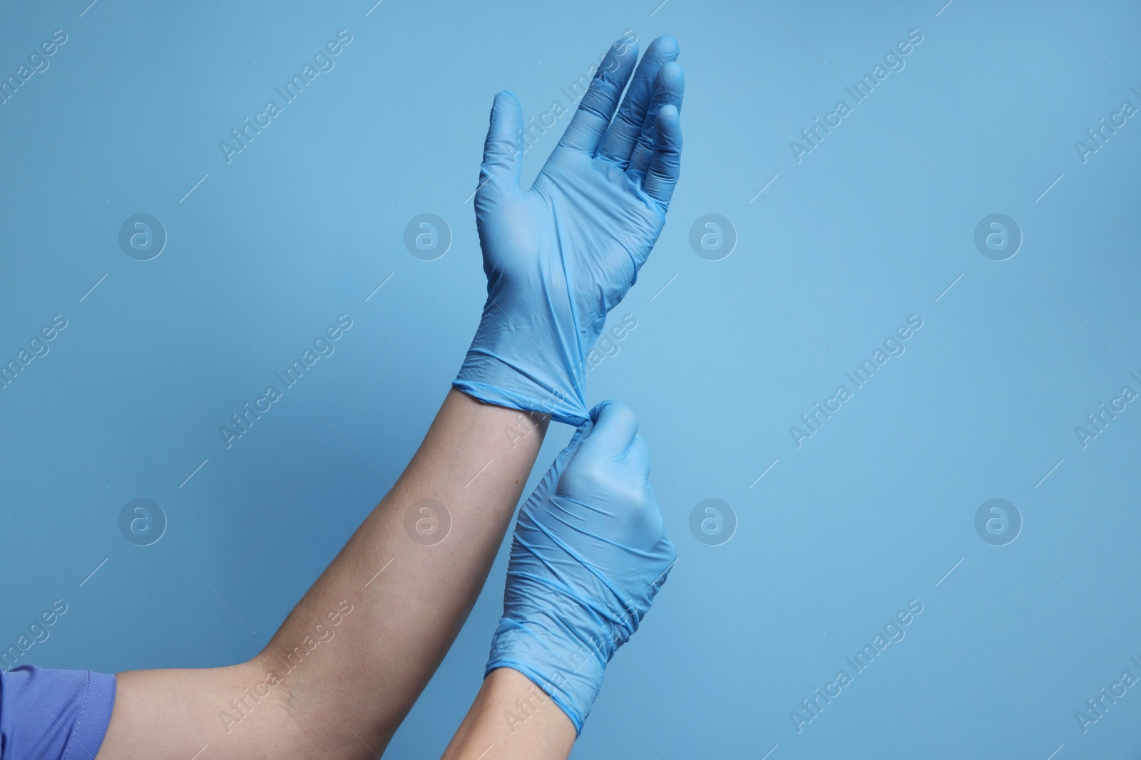 Photo of Doctor wearing medical gloves on light blue background, closeup