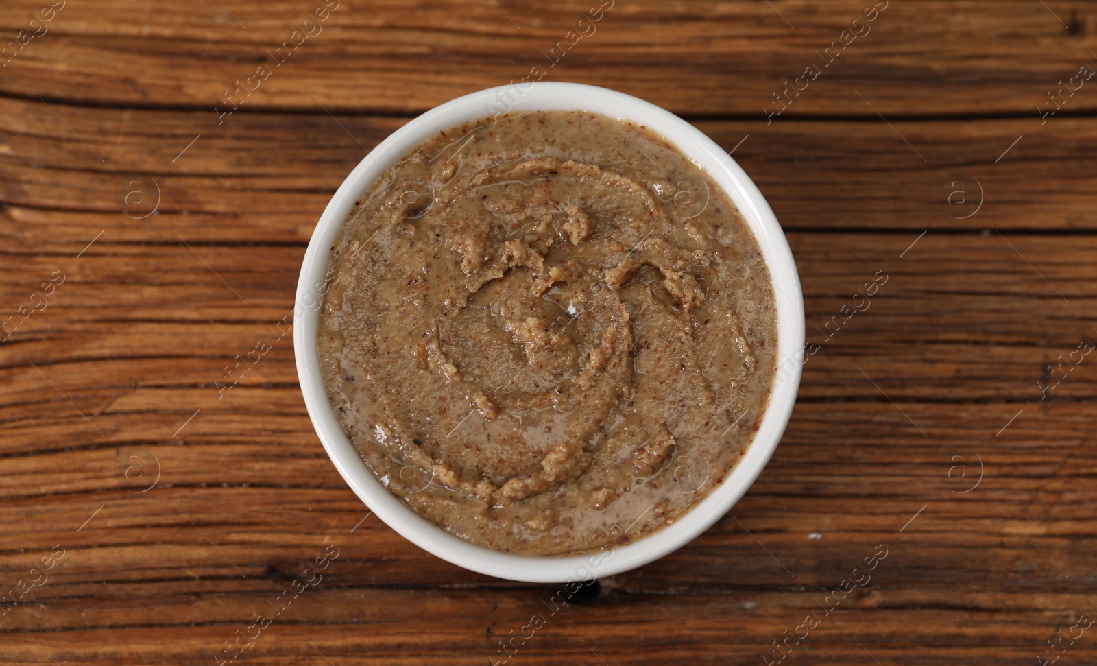 Photo of Delicious nut butter in bowl on wooden table, top view