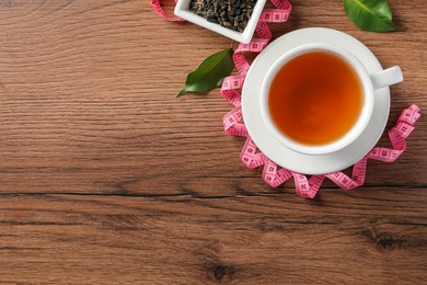 Photo of Cup of herbal diet tea and measuring tape on wooden table, flat lay with space for text. Weight loss concept