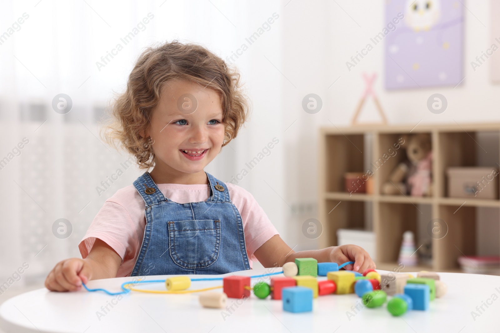 Photo of Motor skills development. Little girl playing with wooden pieces and string for threading activity at table indoors