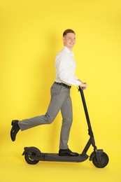 Happy man riding modern electric kick scooter on yellow background