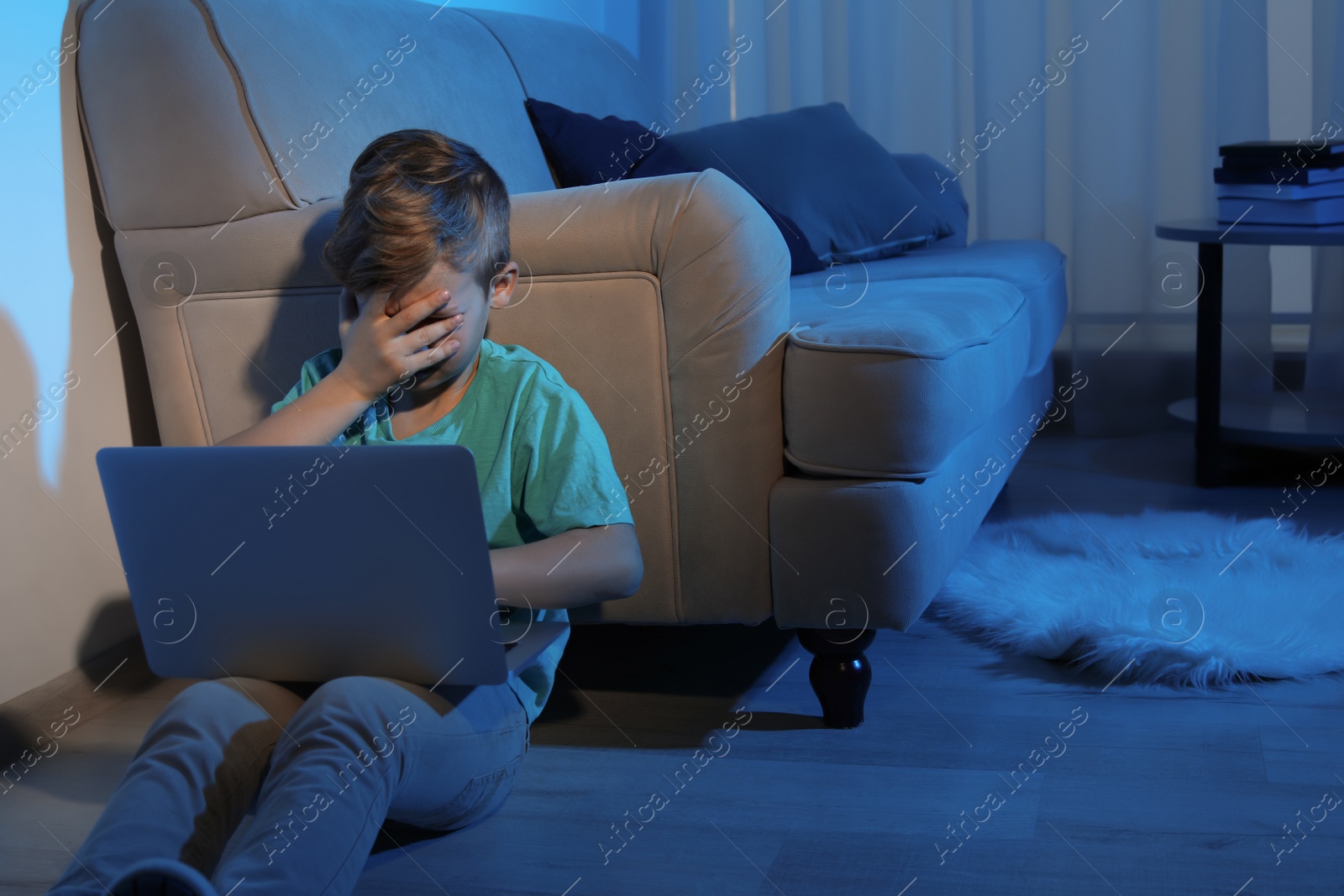 Photo of Frightened little child with laptop in dark room. Danger of internet