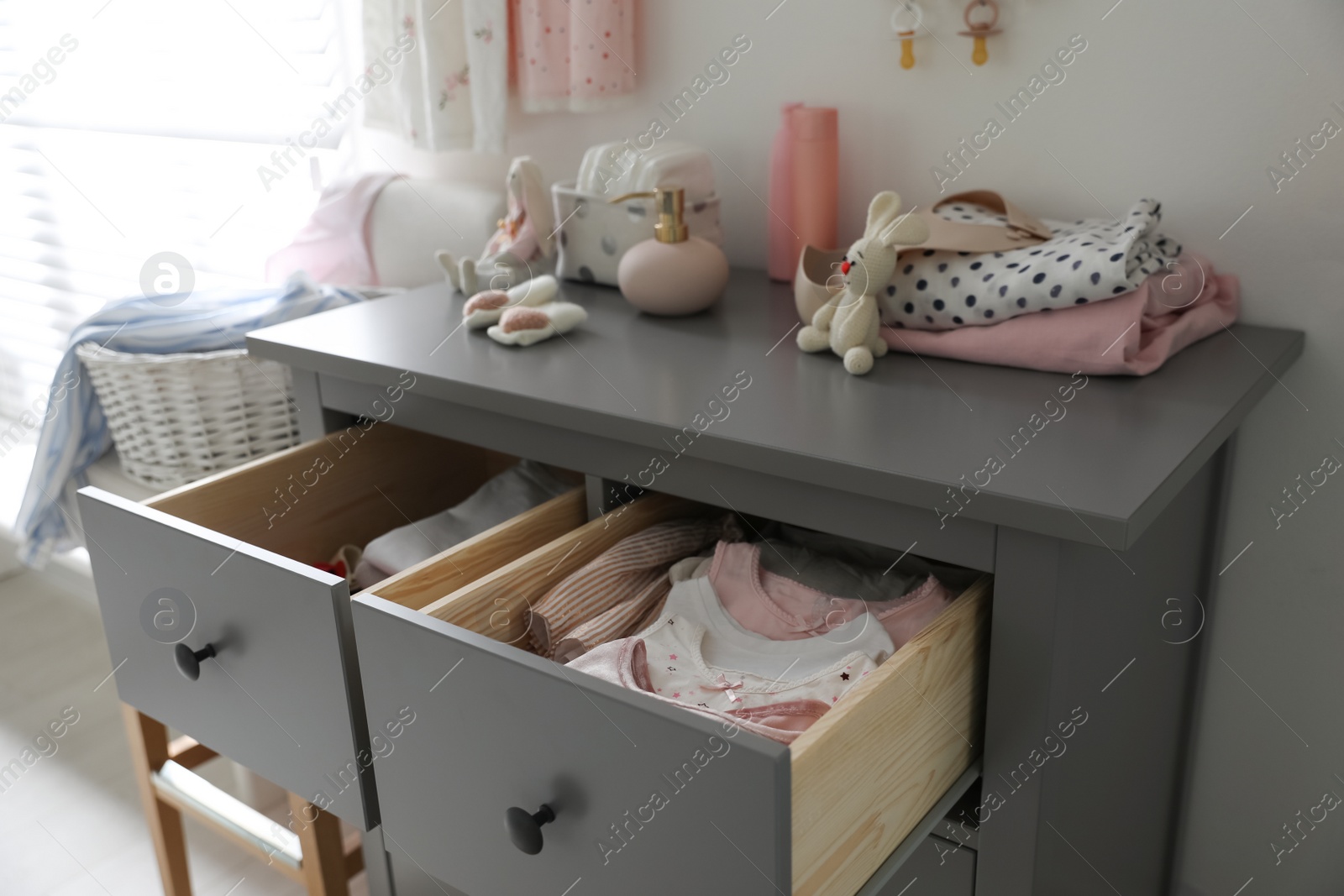 Photo of Open cabinet drawers with baby clothes in child room