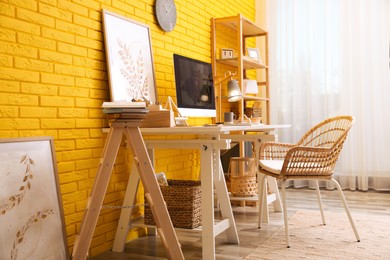 Stylish home office interior with comfortable workplace near yellow brick wall