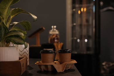 Photo of Takeaway coffee cups with cardboard holder on wooden table indoors