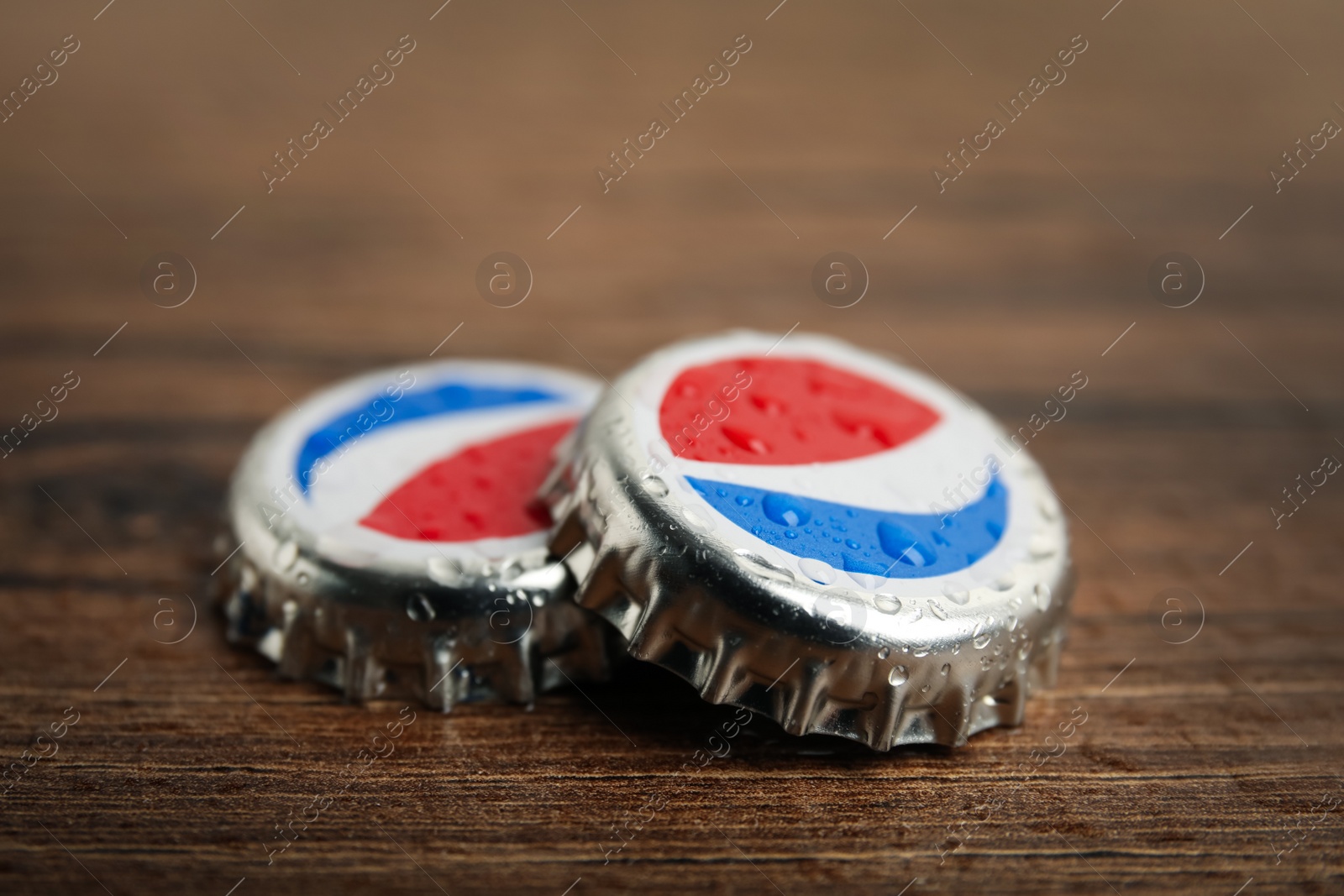 Photo of MYKOLAIV, UKRAINE - FEBRUARY 11, 2021: Pepsi lids with water drops on wooden background, closeup