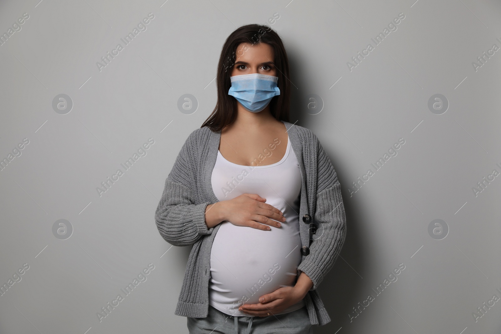 Photo of Young pregnant woman in medical mask on grey background