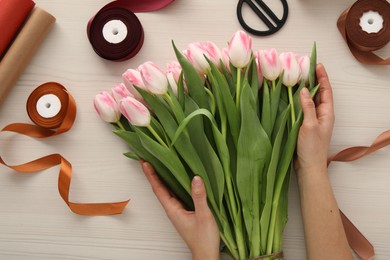 Photo of Woman making bouquet of beautiful fresh tulips at white wooden table, top view