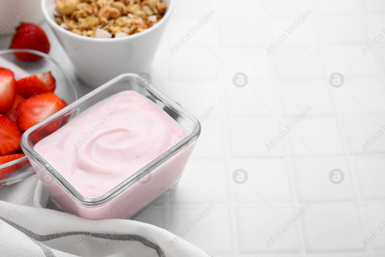 Photo of Delicious yogurt in glass bowl on white tiled table, closeup with space for text. Healthy breakfast