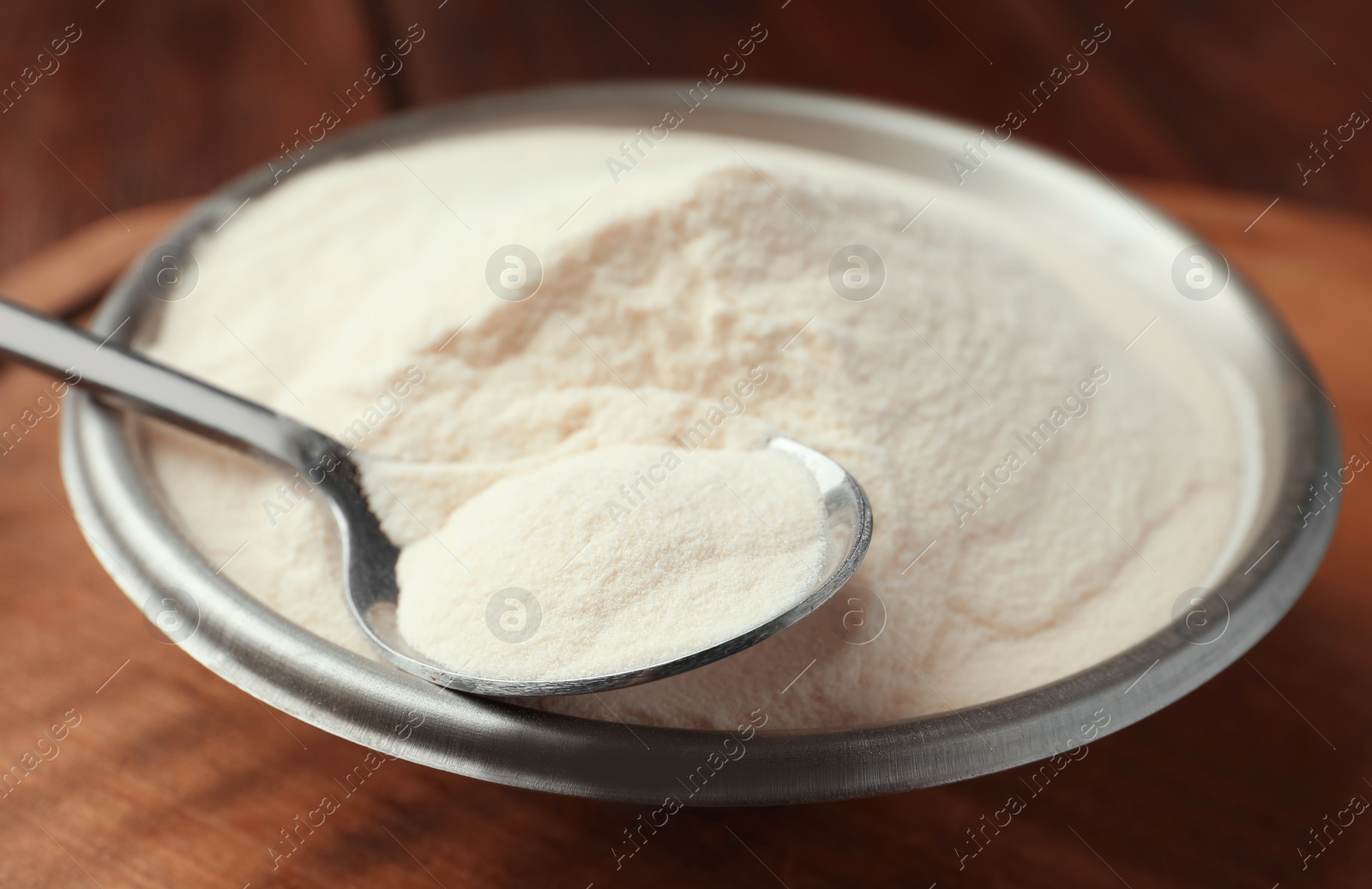 Photo of Bowl and spoon of agar-agar powder on wooden table, closeup