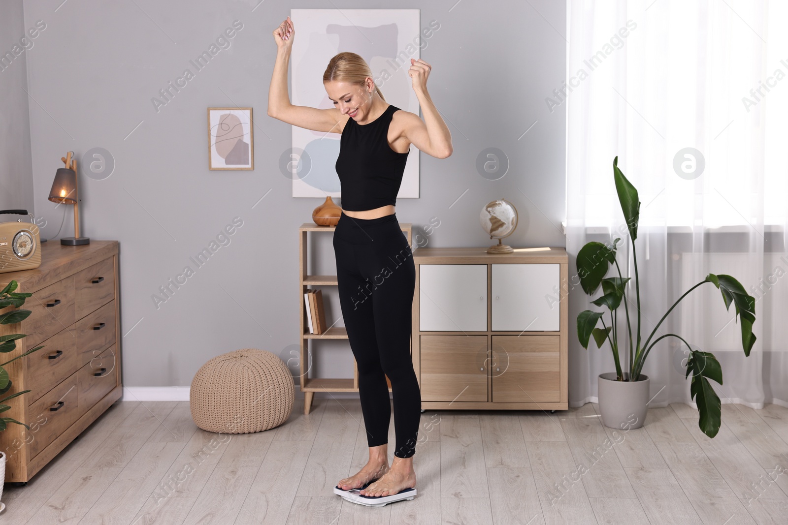 Photo of Happy woman standing on floor scale at home