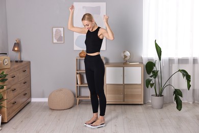 Photo of Happy woman standing on floor scale at home