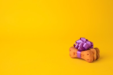 Photo of Bone shaped dog cookies with purple bow on yellow background. Space for text