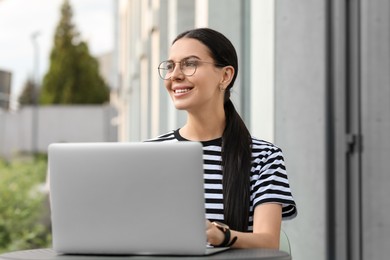 Photo of Happy young woman using modern laptop at table outdoors