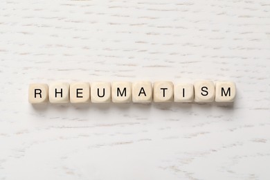 Photo of Cubes with word Rheumatism on white wooden table, flat lay