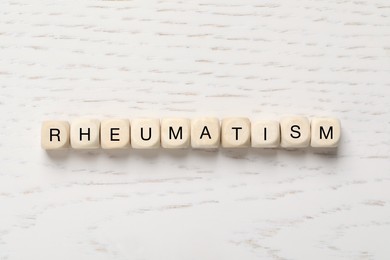 Cubes with word Rheumatism on white wooden table, flat lay