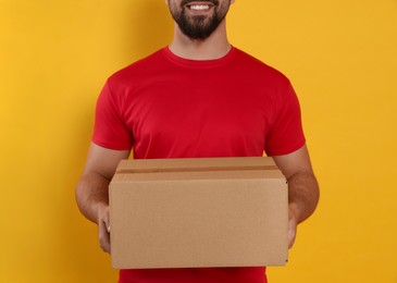 Photo of Courier holding cardboard box on yellow background, closeup