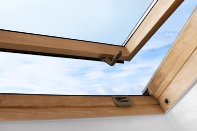 Photo of Beautiful view of cloudscape from open skylight roof window on slanted ceiling. Attic room