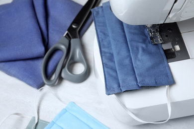 Photo of Sewing machine with homemade protective mask on table, closeup