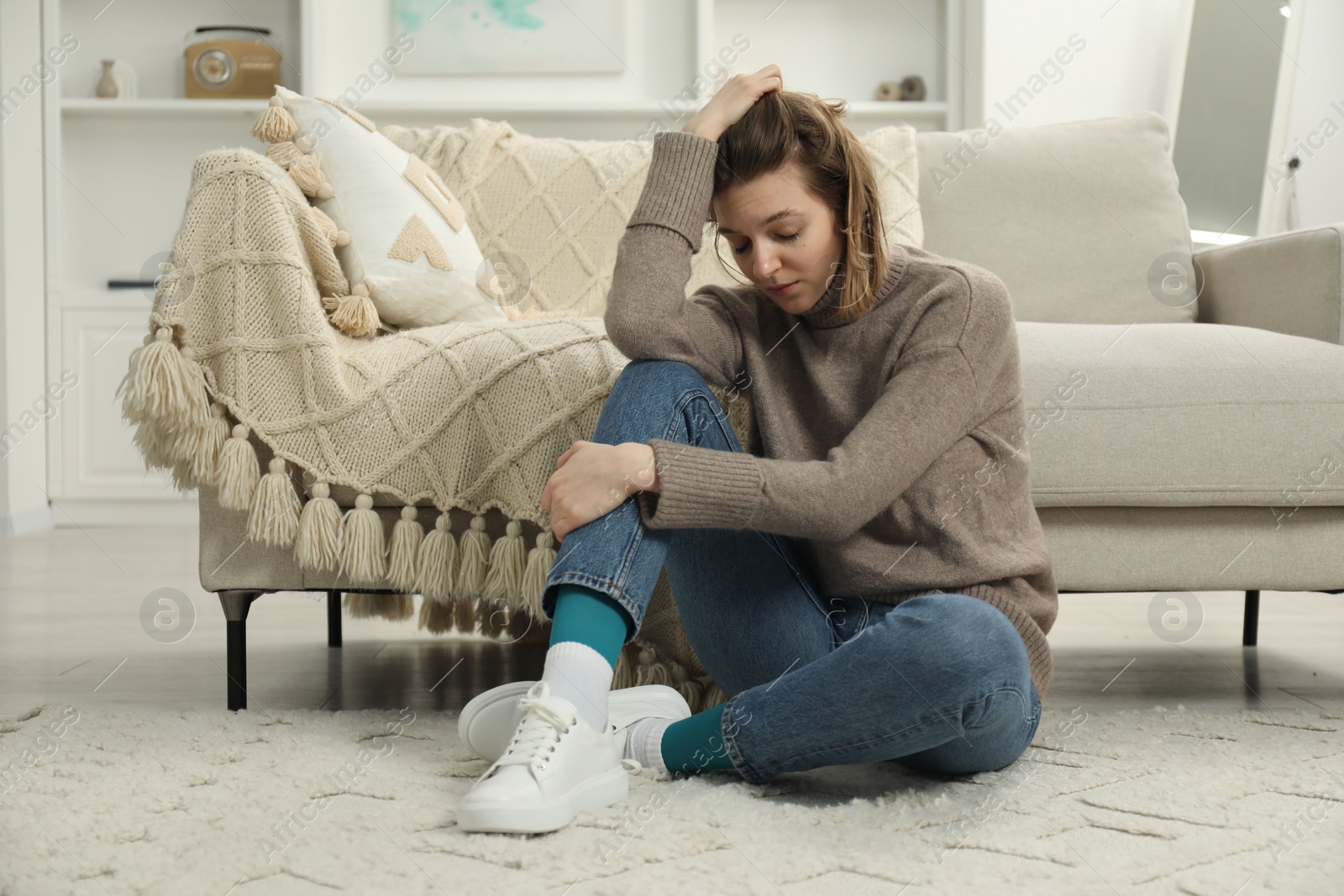 Photo of Sad young woman sitting on floor at home