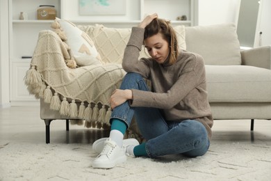 Sad young woman sitting on floor at home