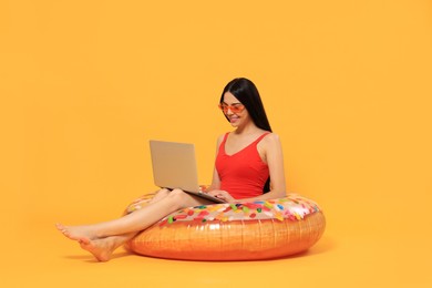 Photo of Happy young woman with beautiful suntan using laptop on inflatable ring against orange background