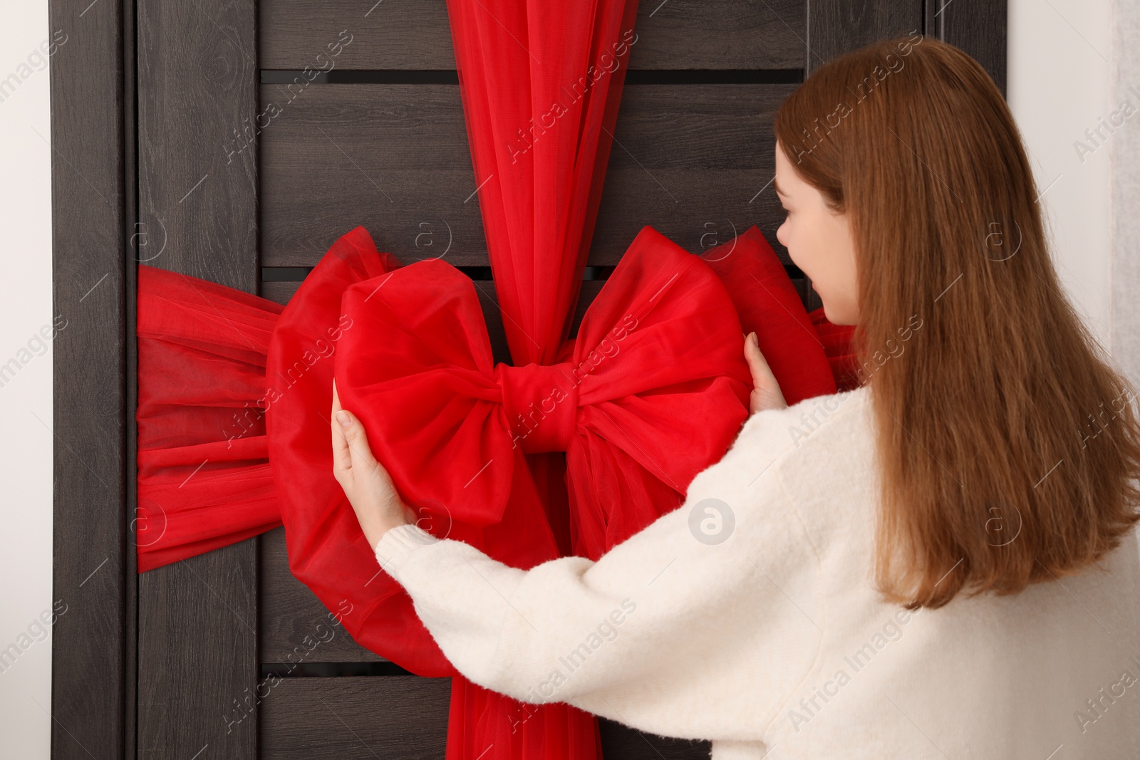 Photo of Woman decorating wooden door with red bow. Christmas mood