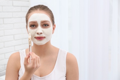 Photo of Beautiful woman applying homemade mask on her face indoors