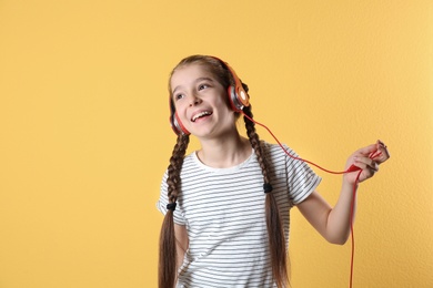 Photo of Cute little girl listening to music with headphones on color background