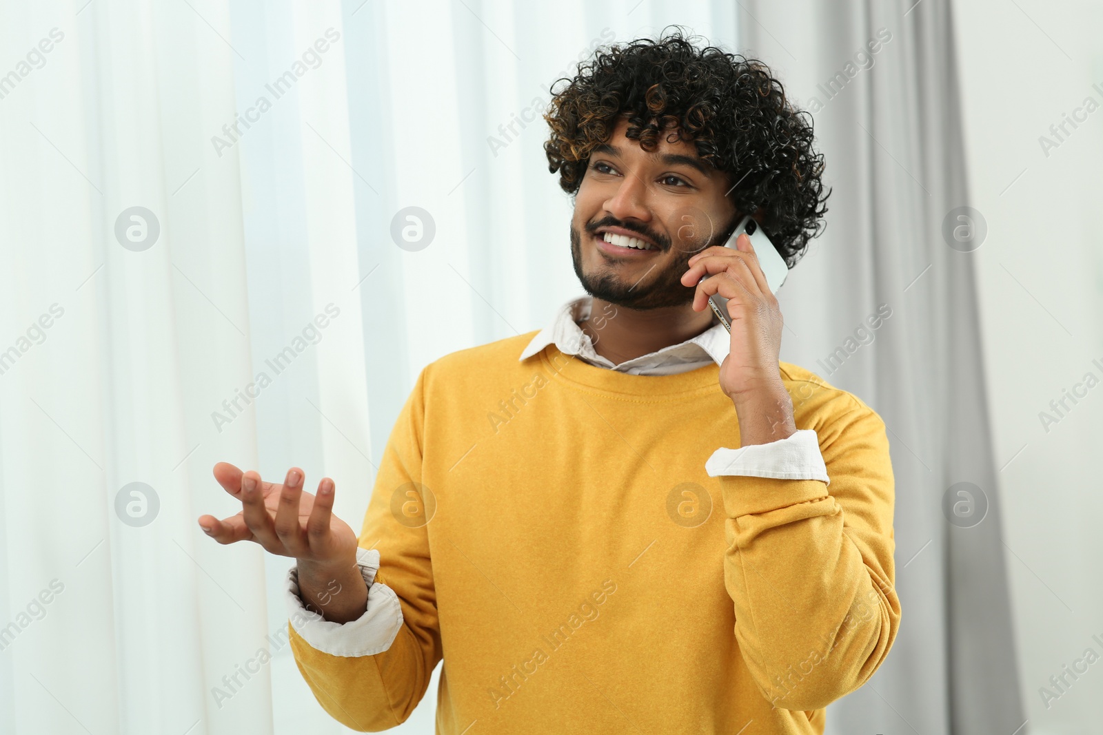 Photo of Handsome smiling man taking over smartphone indoors