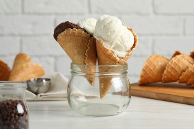 Ice cream scoops in wafer cones on white wooden table against brick wall