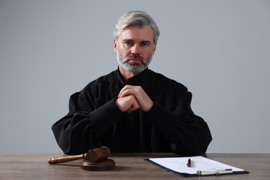 Photo of Judge with gavel and papers sitting at wooden table against light grey background