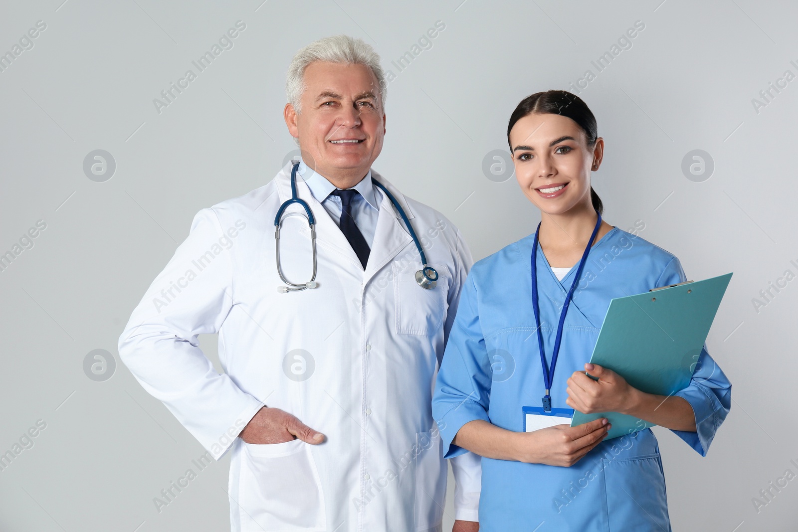 Photo of Senior doctor and young nurse against light background