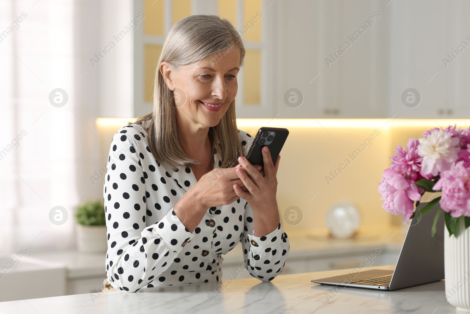 Photo of Senior woman using mobile phone at white table indoors