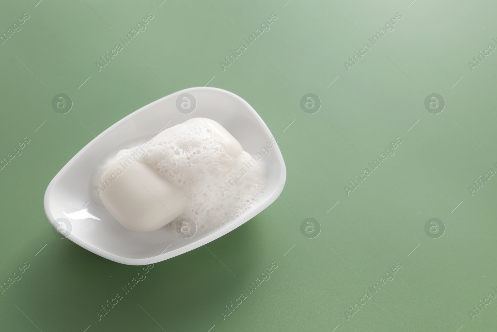 Photo of Dish with soap bar and fluffy foam on green background, space for text