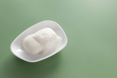 Dish with soap bar and fluffy foam on green background, space for text