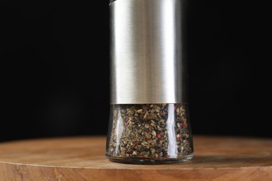 Photo of Pepper shaker on wooden board against black background, closeup
