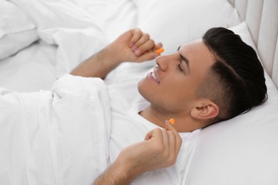 Photo of Man inserting foam ear plugs in bed