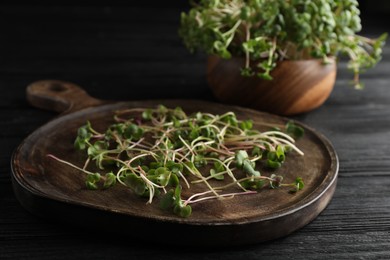 Board with cut fresh radish microgreens on black wooden table, closeup