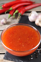 Spicy chili sauce in bowl and ingredients on wooden table, closeup